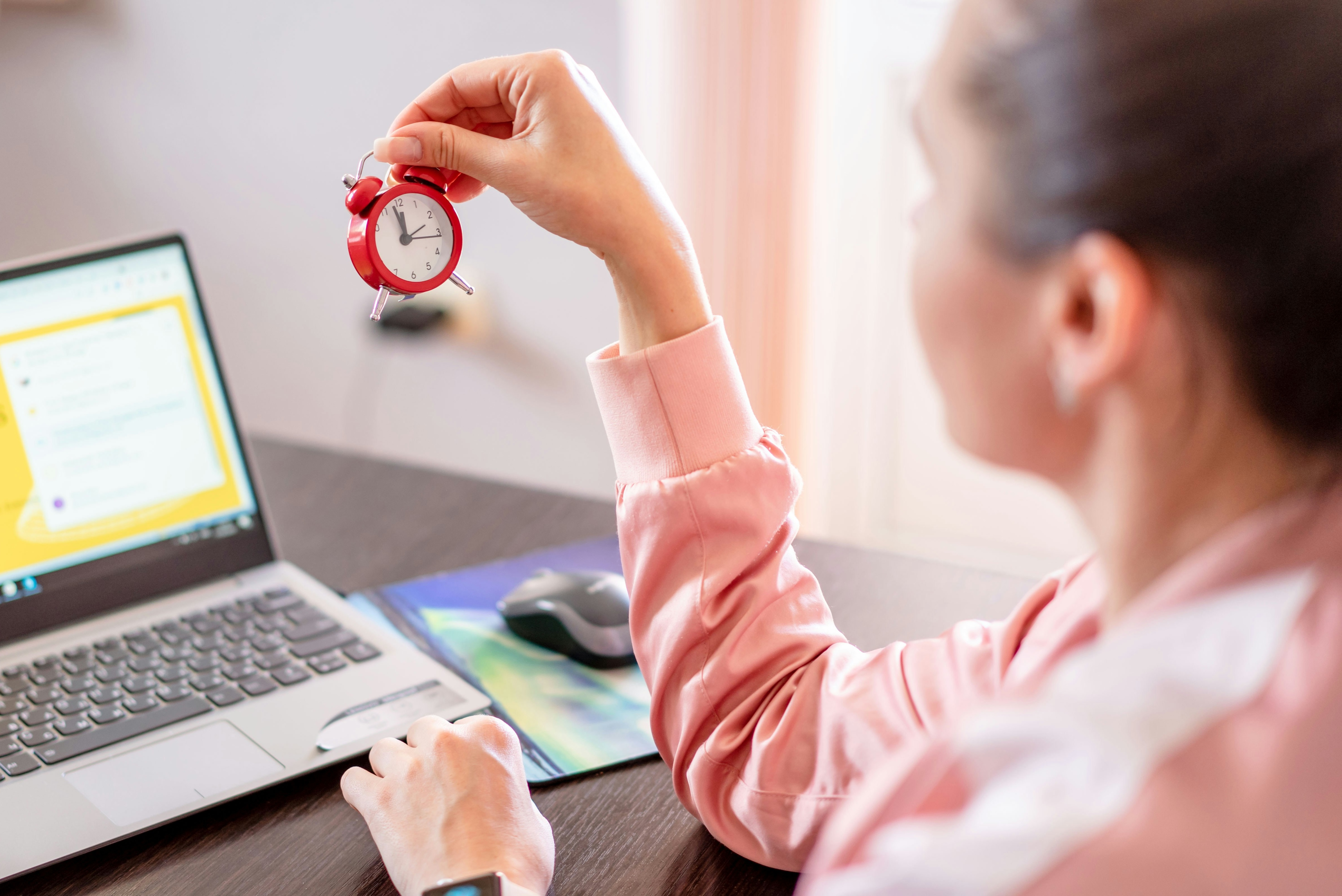 a woman at a laptop holding a clock